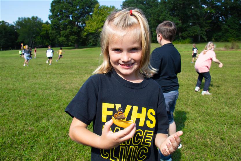 A girl wearing a black t-shirt holds a butterfly on an orange slice